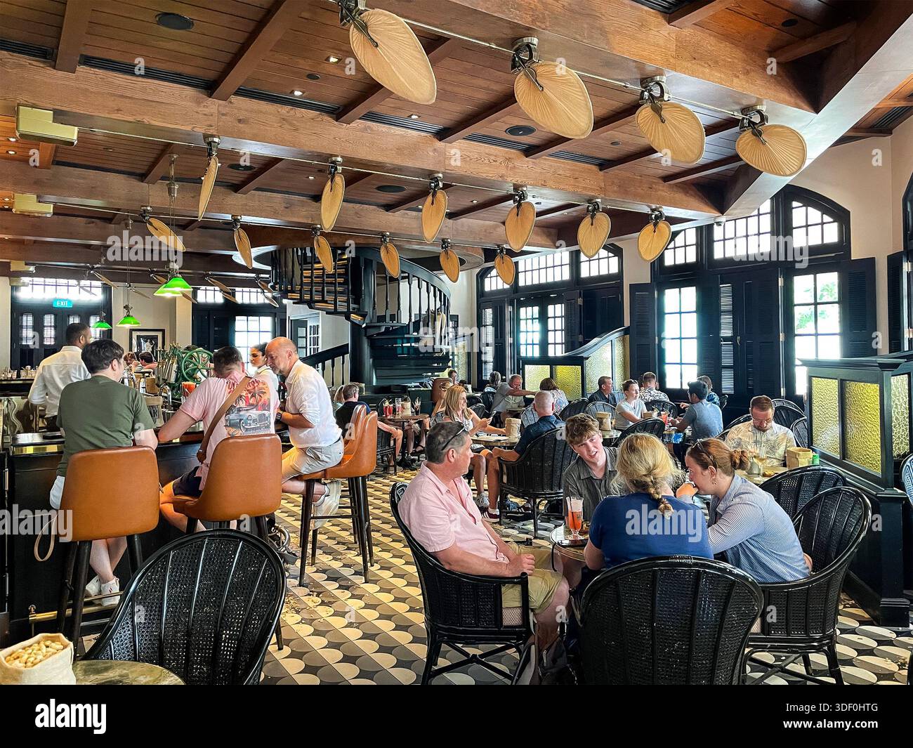 Die Long Bar im historischen Raffles Hotel in Singapur bietet Gästen Speisen und Trinken singapur, Cocktails, Deckenventilatoren und gemusterte Fliesenböden Stockfoto