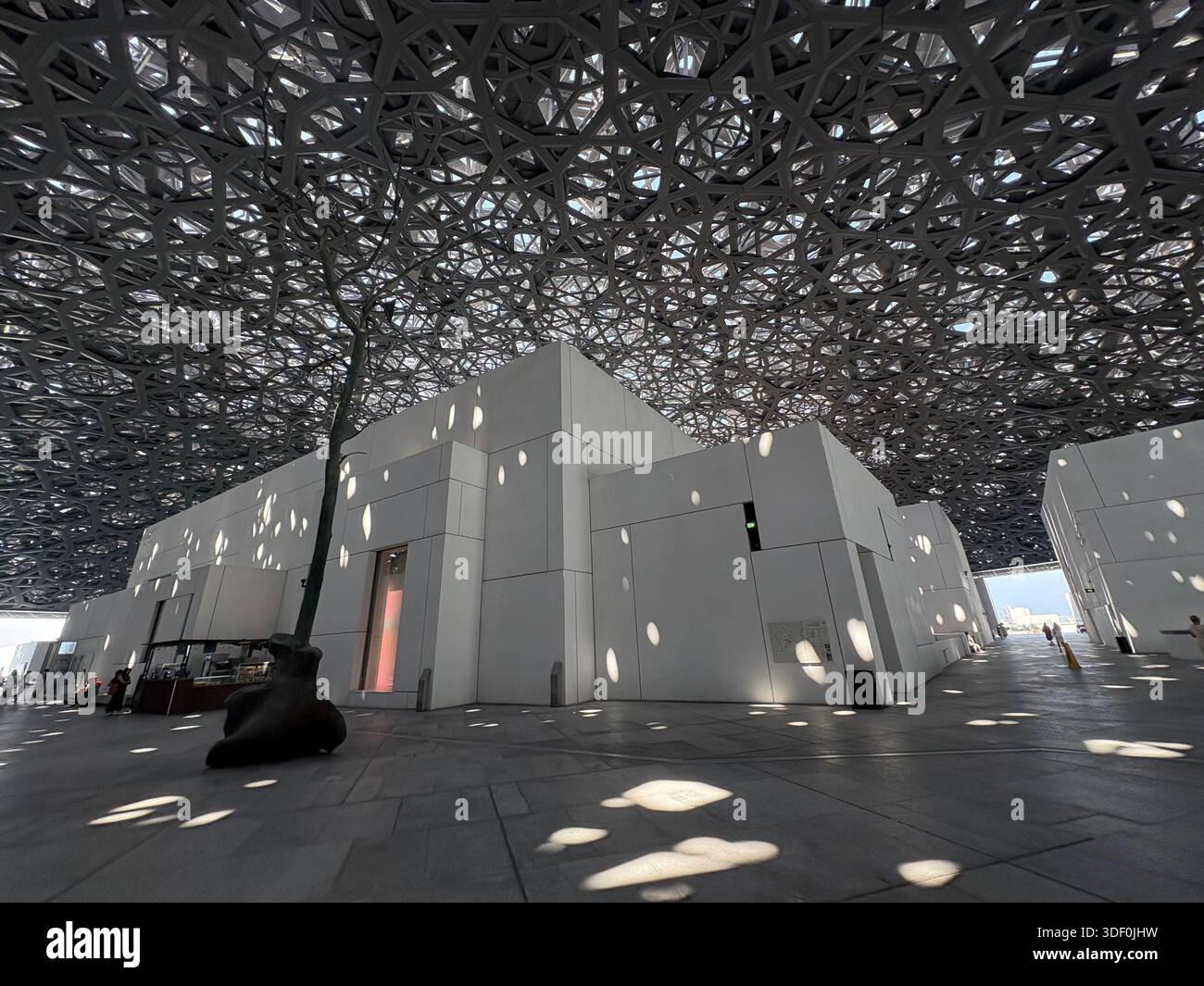 Die berühmte Kuppel des Louvre Abu Dhabi wirft einen faszinierenden Lichtregen über den ruhigen Innenhof Stockfoto