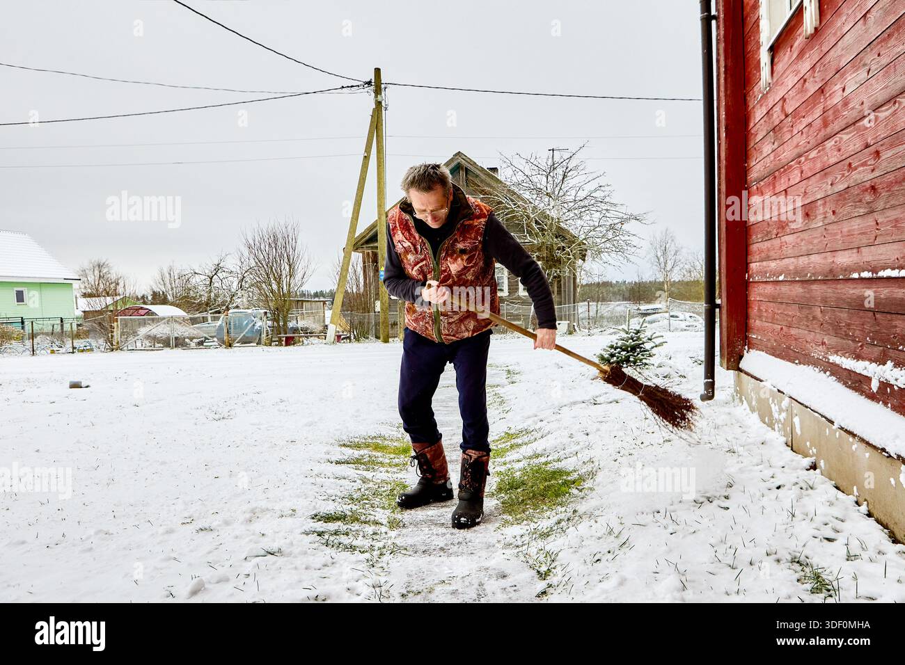 Der Mann um 50 kehrt nach Schneefall den Gartenweg. Stockfoto