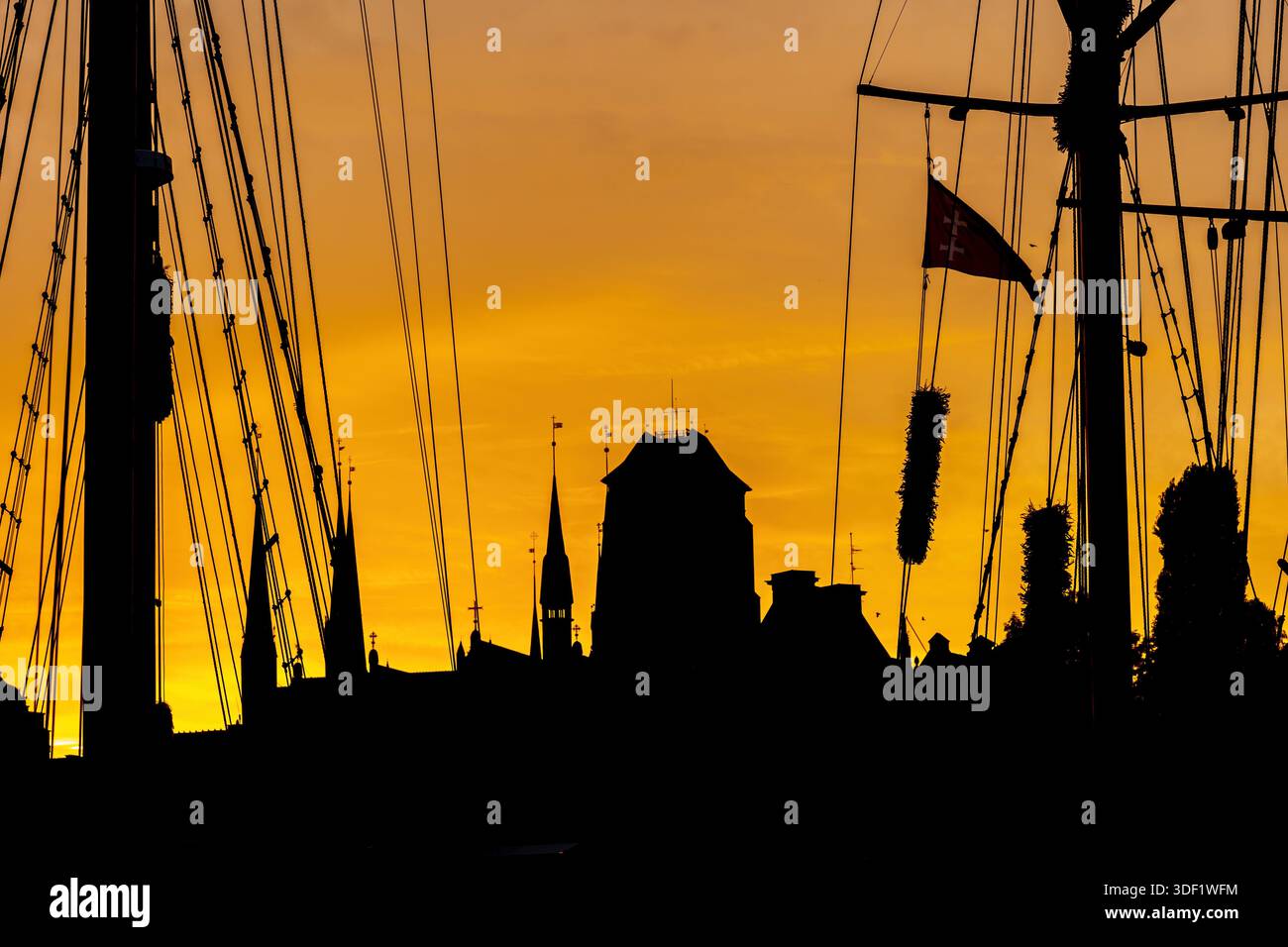 Silhouette bei Sonnenuntergang mit Masten und Seilen von Segelbooten in der Altstadt von Danzig, Hafenstadt in Polen. Skyline mit Türmen und Turm von St. Mary Basi Stockfoto
