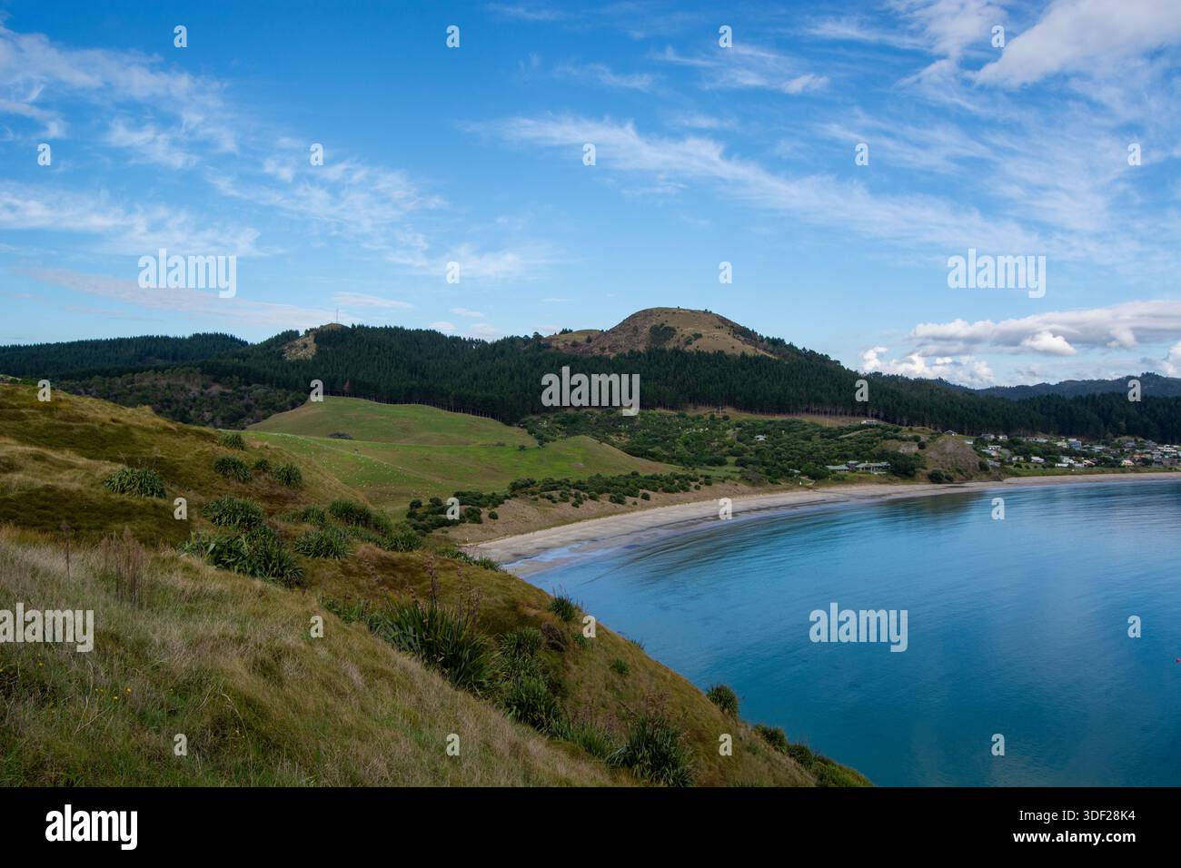 Eine ruhige Küstenlandschaft mit einer ruhigen Bucht, Sandstrand und sanften grünen Hügeln unter einem klaren blauen Himmel. Die Szene fängt die Schönheit der Natur ein Stockfoto