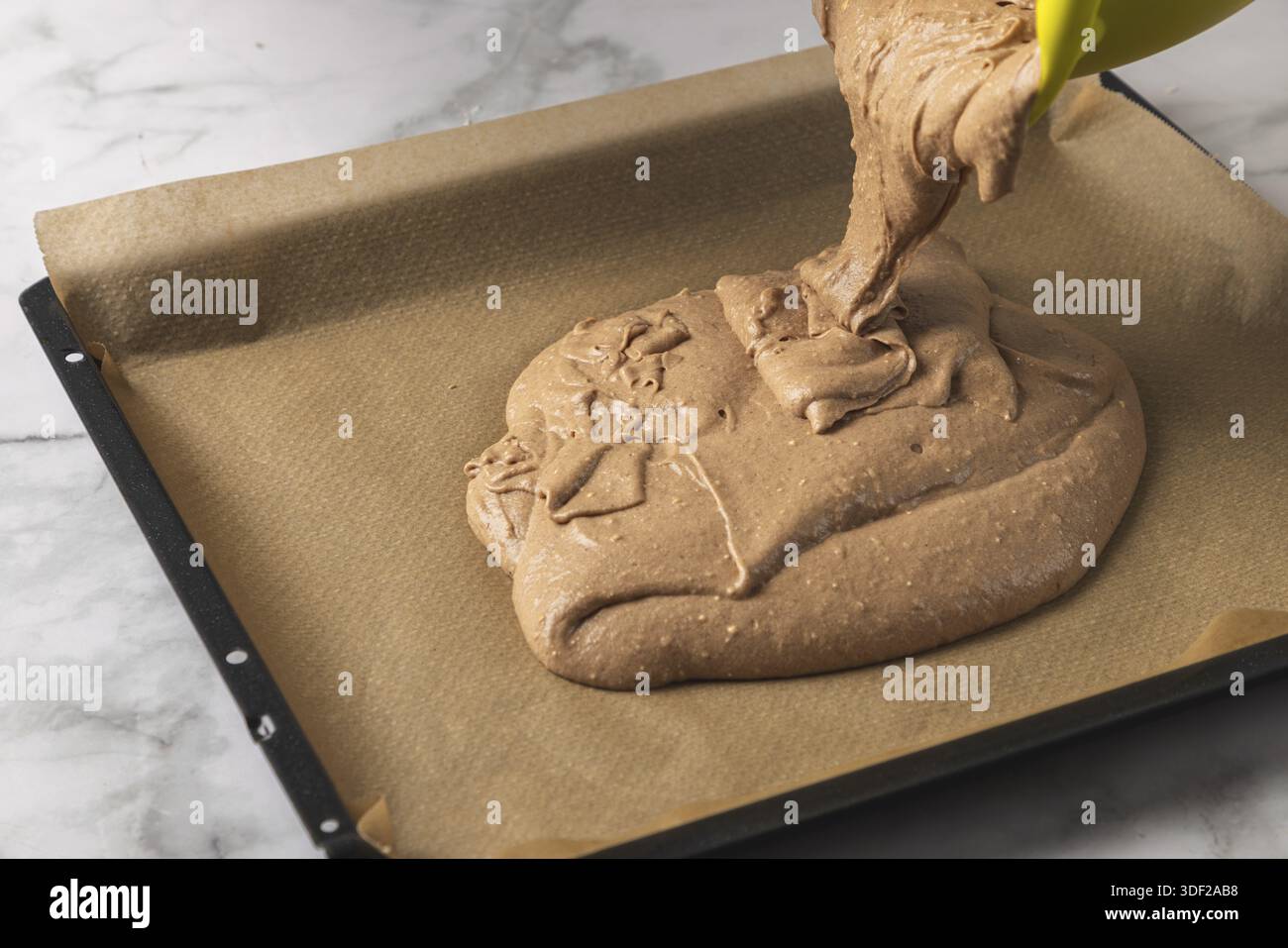 Der Kakaoteig wird auf ein mit Backpapier ausgelegtes Backblech gegossen Stockfoto