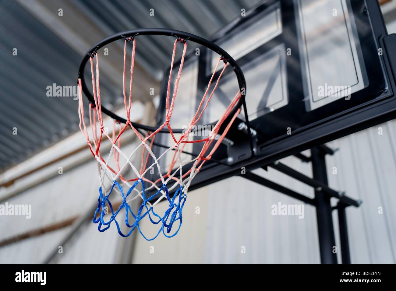 Nahaufnahme des Basketballrandes und des Trikolore-Netzes an der Rückwand, das die Details der Sportausrüstung zum Training und zur Freizeitaktivität hervorhebt Stockfoto