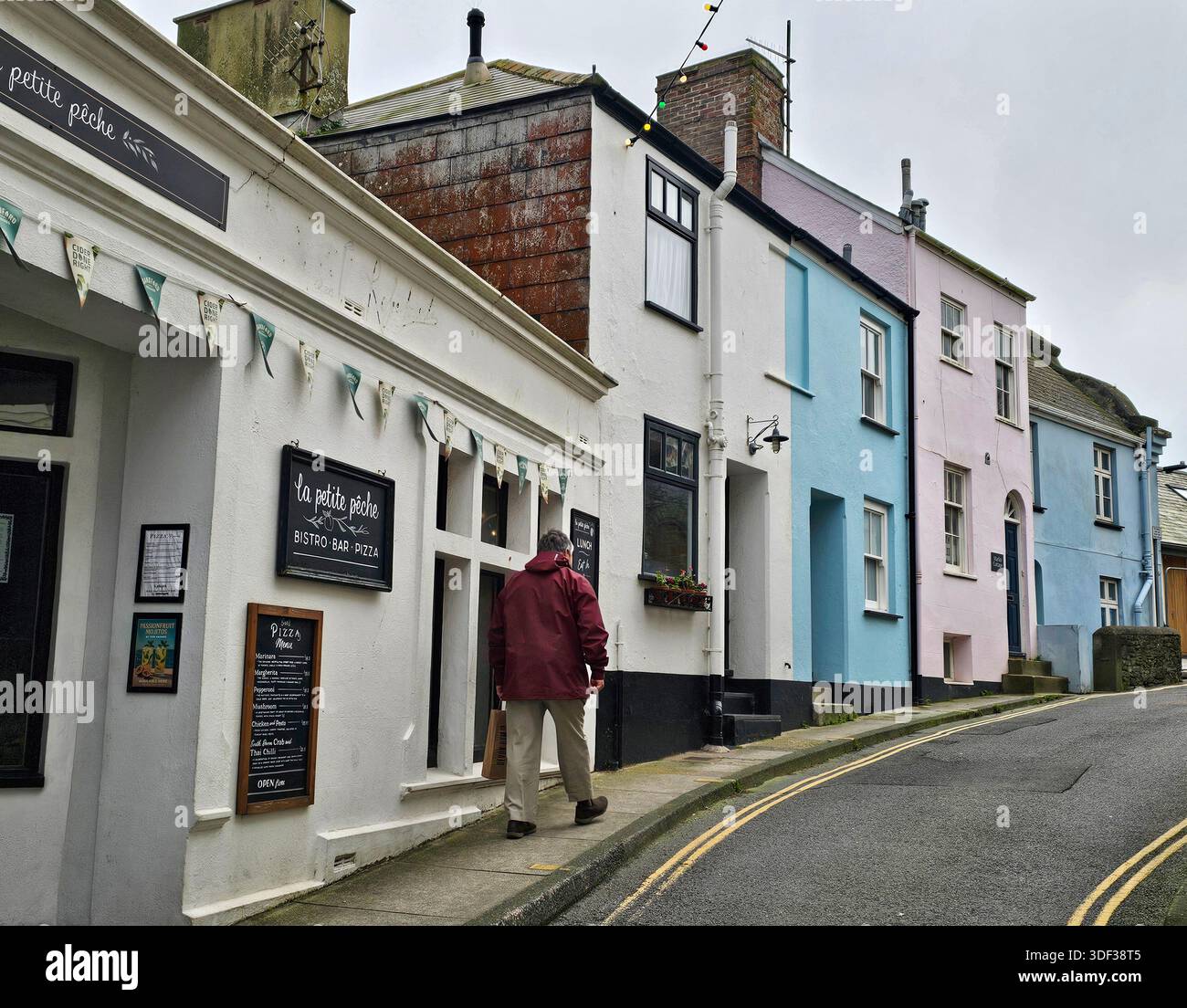 Ein Mann läuft die Fore Street hoch, vorbei an einem Pizzarestaurant in Salcombe, Devon - Smartphone-aufgenommenes Stockfoto