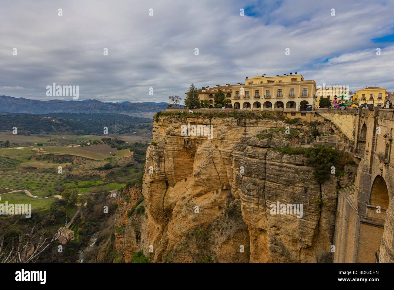 Besucher bewundern atemberaubende Ausblicke von der Klippe in Ronda, Spanien, mit grünen Hügeln und Bergen, die die Szene umrahmen. Stockfoto