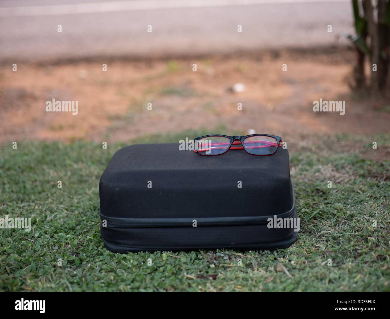 Die Brille liegt auf einem Hartschalenkoffer auf dem Gras und steht für Sehpflege und persönliches Zubehör im Freien. Stockfoto