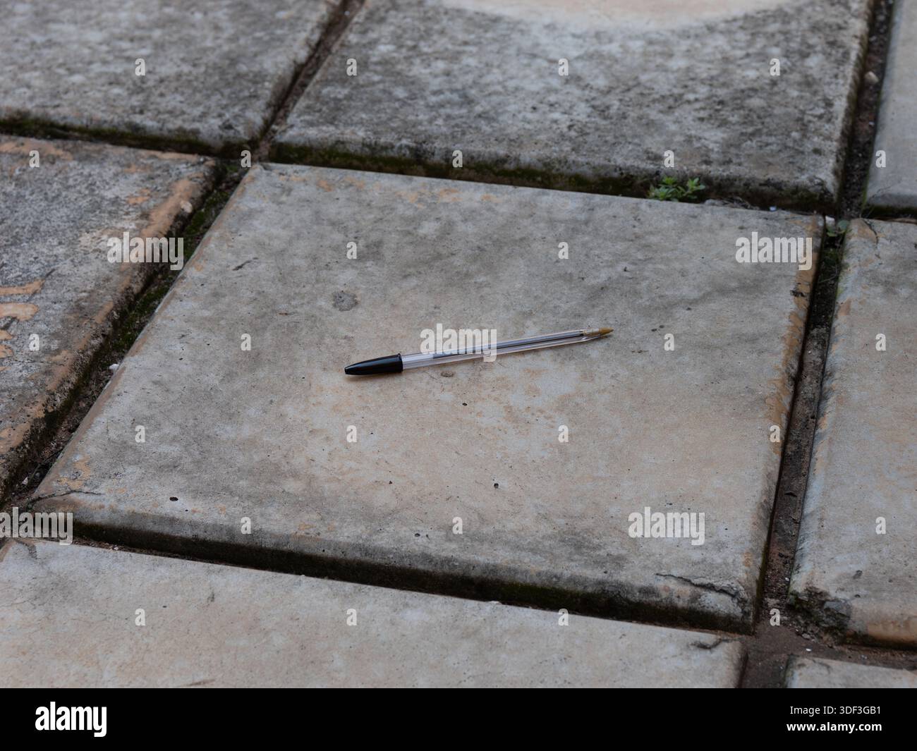 Kugelschreiber auf Betonpflaster im Freien, der ein vergessenes Schreibgerät in einer urbanen Umgebung darstellt. Stockfoto