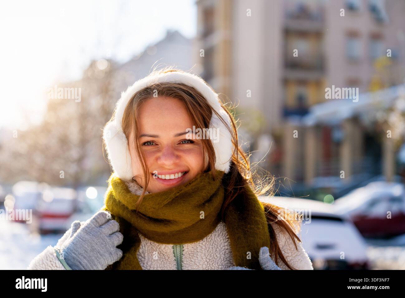 Junge Frau mit Ohrenschützern und warmem Schal, die draußen an einem sonnigen Wintertag steht. Stockfoto