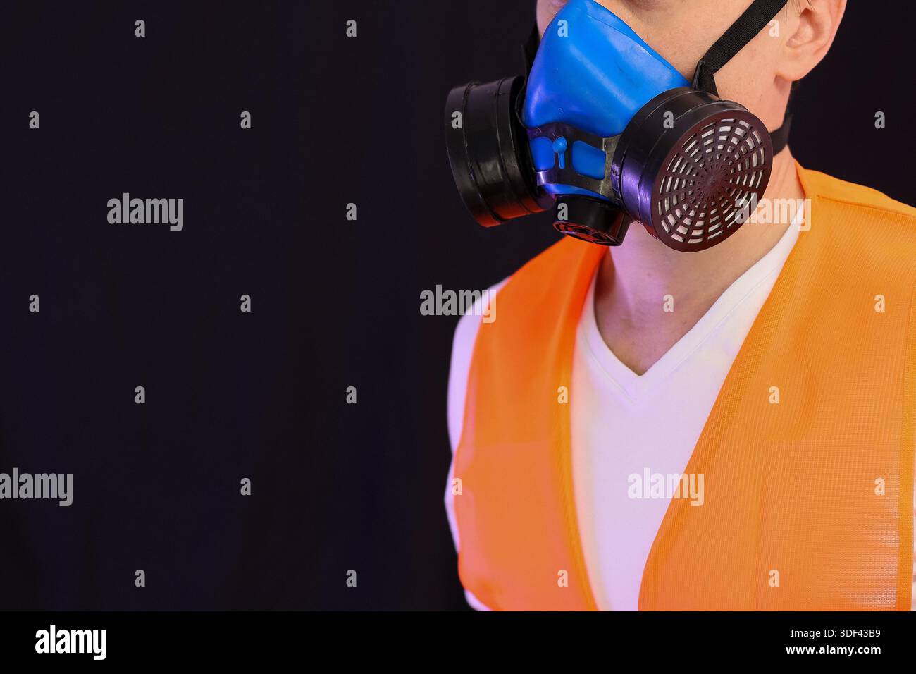 Profilaufnahme einer Person in Sicherheitsweste mit blauer Atemschutzmaske vor dunklem Hintergrund Stockfoto