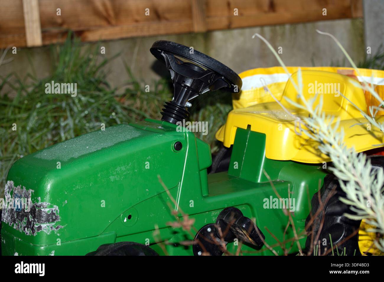 Verwitterter grüner und gelber Aufsitzspielzeugtraktor in Garteneinstellung Stockfoto