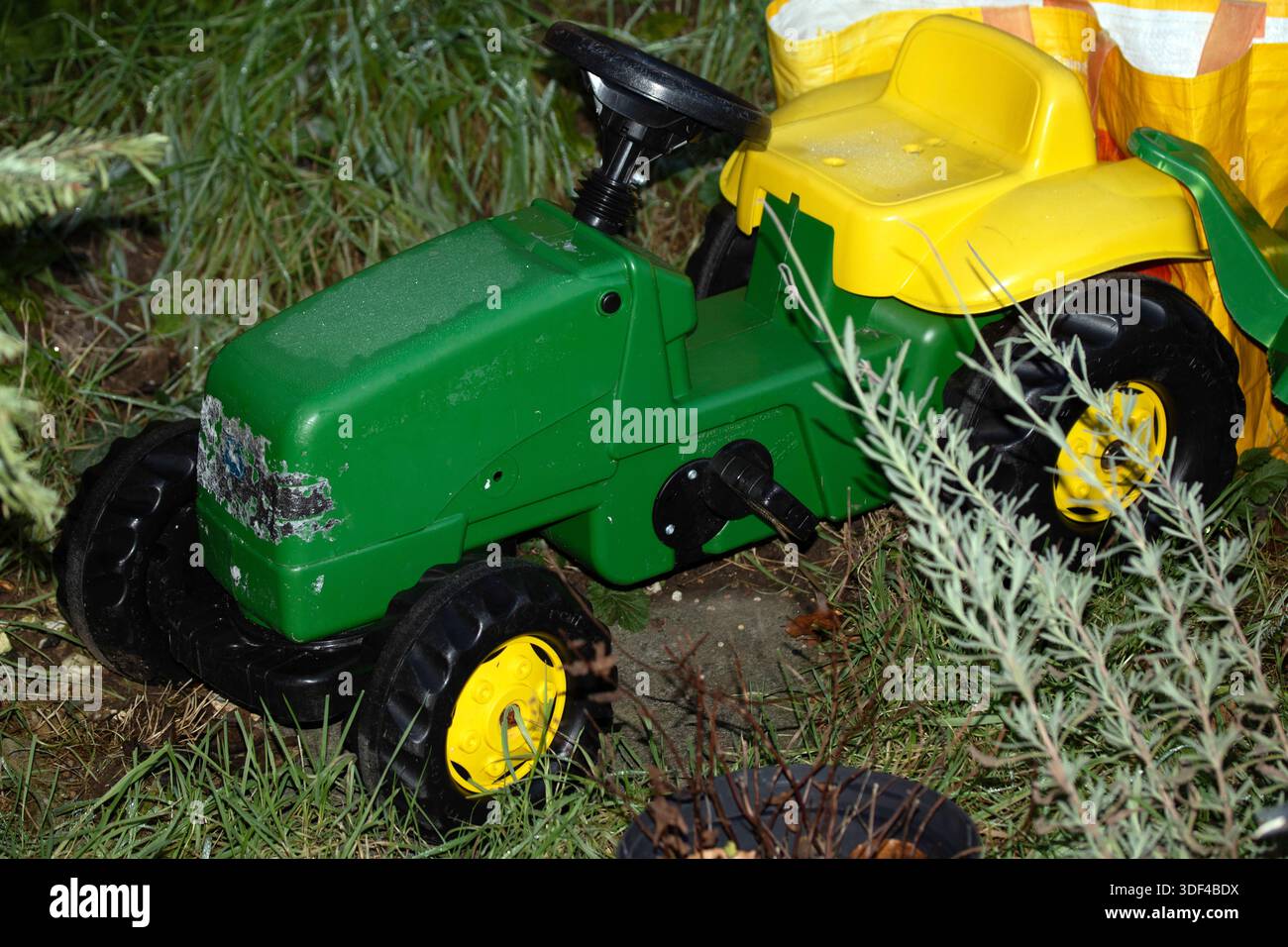 Verwitterter grüner und gelber Aufsitzspielzeugtraktor in Garteneinstellung Stockfoto