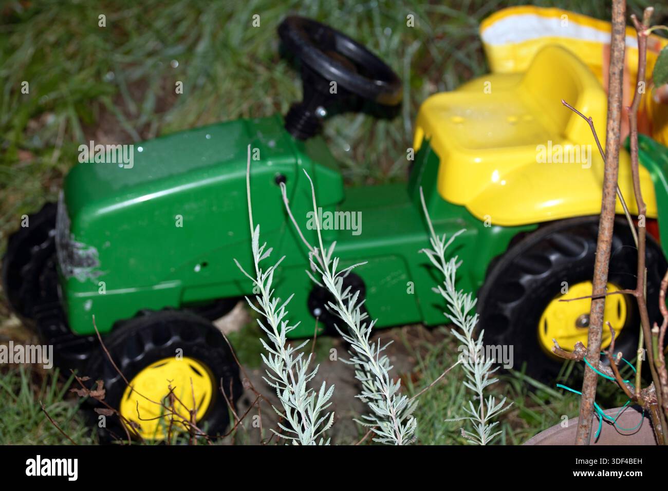 Verwitterter grüner und gelber Aufsitzspielzeugtraktor in Garteneinstellung Stockfoto
