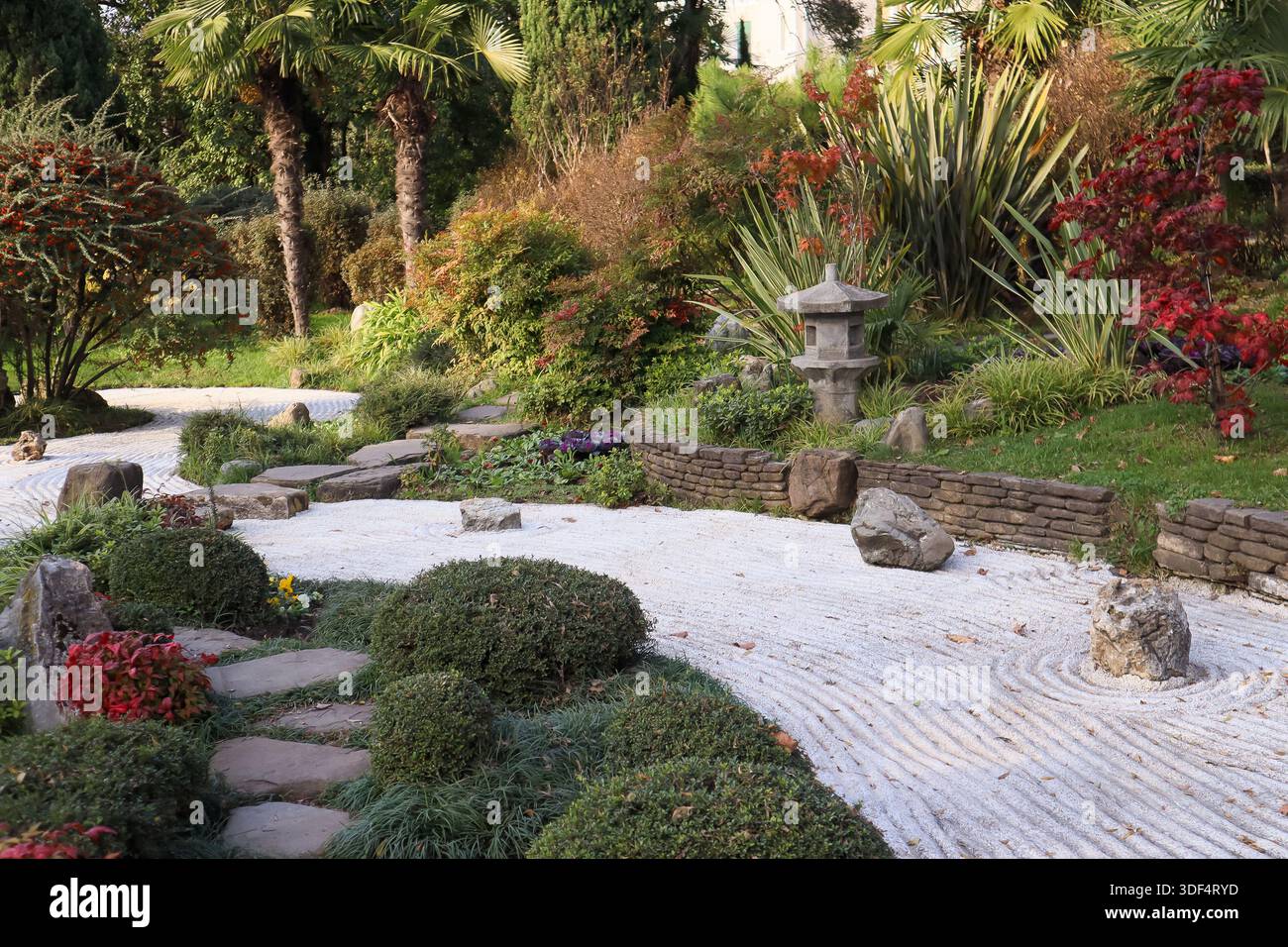 Traditioneller japanischer Zen-Garten mit Steinlaternen, geharktem Kies wirbelt um Felsen, immergrünen Sträuchern, bunten Herbstahorn und üppigem Grün Stockfoto