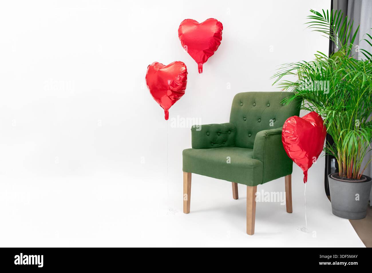 Ein grüner Sessel, umgeben von roten Herzballons in einem weißen Innenraum, romantisch, elegant und mit Kopierraum Stockfoto