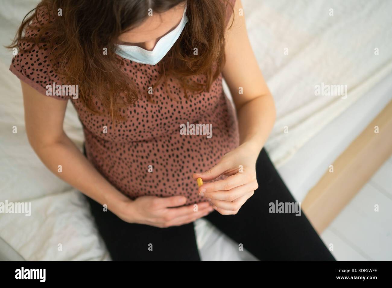 Draufsicht einer schwangeren Frau mit einer Pille in der Hand. Symbol für Pflege, Gesundheit und Unterstützung während der Mutterschaft. Stockfoto