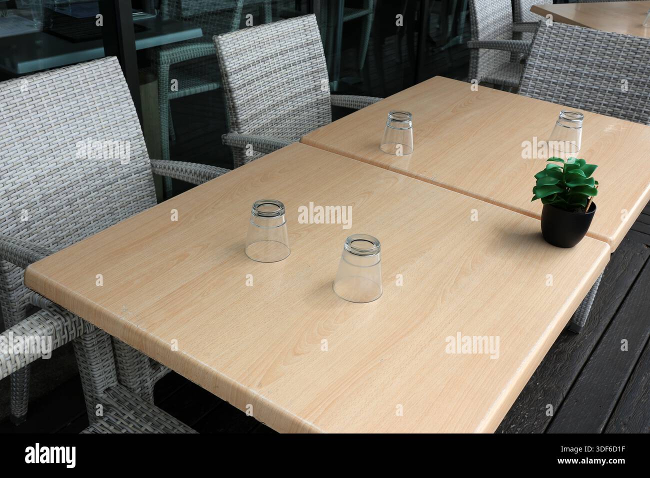 Essen im Freien mit einem Holztisch, Stühlen, Trinkgläsern und einer Topfpflanze Stockfoto