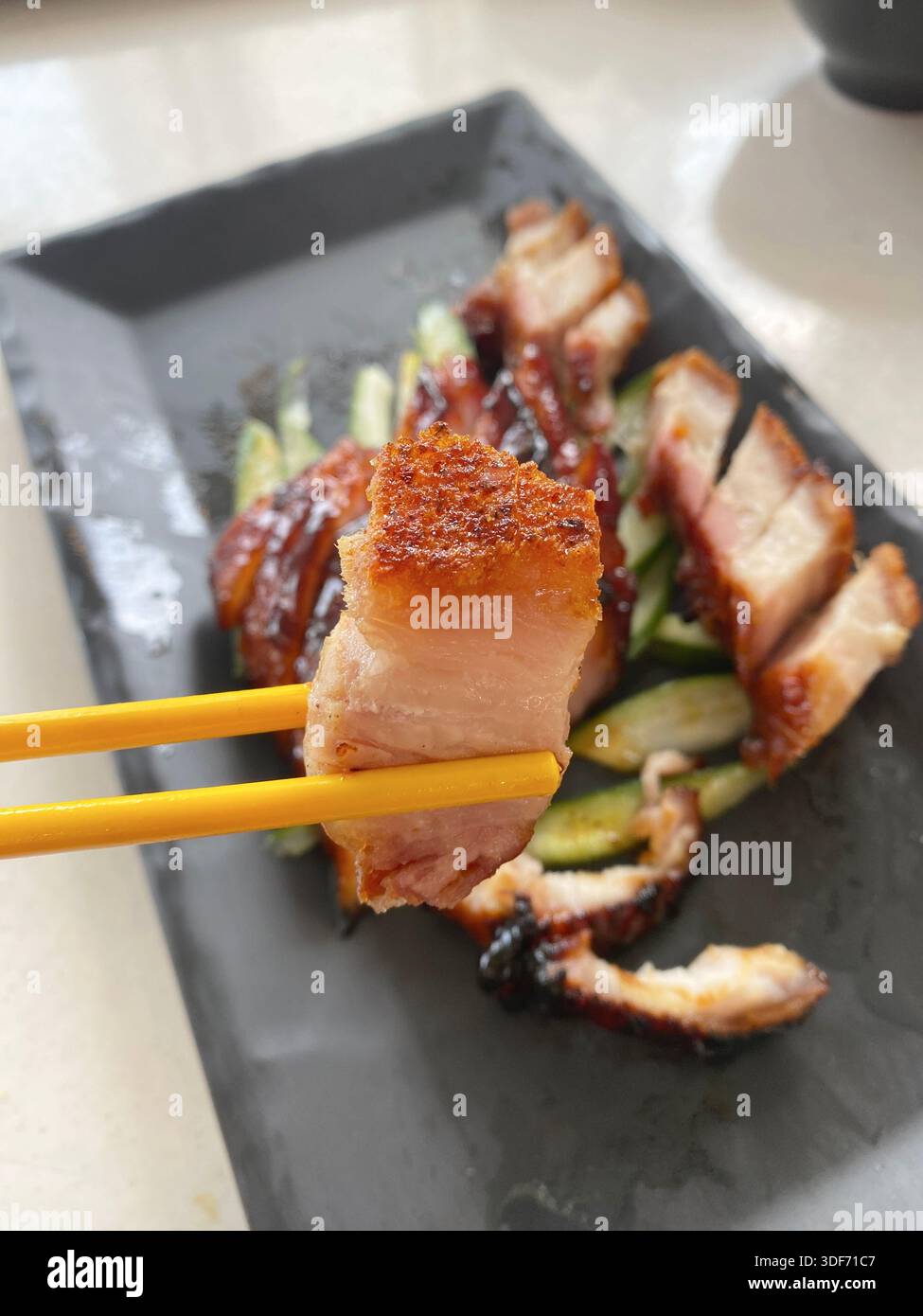 Geschlossener Schuss von gebratenem Schweinefleisch nach kantonesischer Art oder Siu Yuk (gebratener Schweinebauch mit knuspriger Haut), aufgenommen von einem Paar Essstäbchen Stockfoto