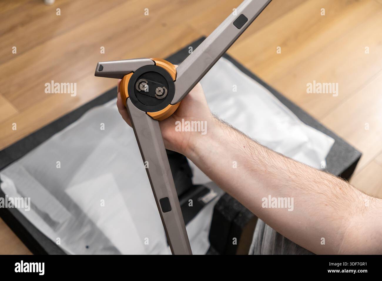 Ansicht einer Hand, die ein graues und orangefarbenes Kamerastativ zusammensetzt, zeigt detaillierte Konstruktion und langlebige Materialien, ideal für professionelle Videos Stockfoto