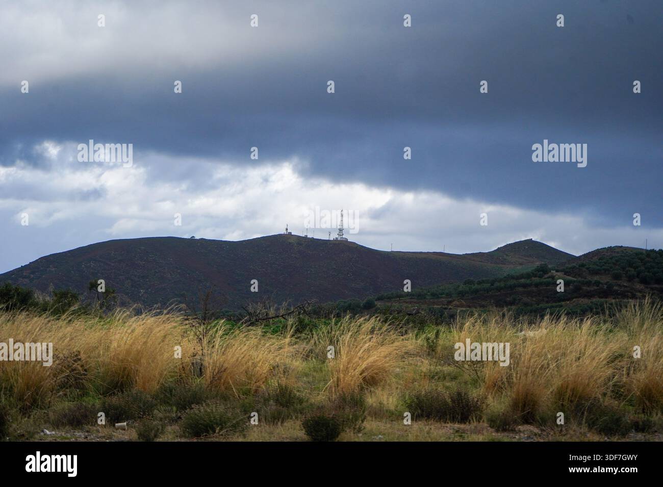 Kommunikationstürme und Antennen auf einem felsigen Bergrücken unter einem dramatischen bewölkten Himmel, mit Blick auf die VOAK-Autobahn zwischen Heraklion und Fodele, Stockfoto