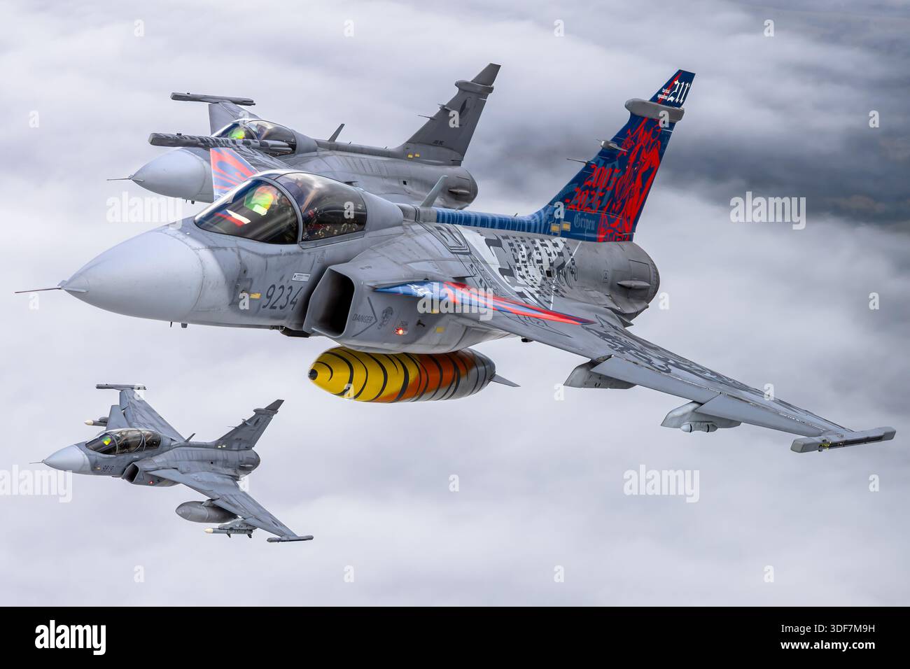 Luft-Luft-Foto, das die tschechischen Luftwaffe Saab JAS 39C und JAS 39D Gripen zeigt, die an den NATO-Tagen 2025 teilnahmen. Das Bild zeigt einsitzige JAS 39C-Jäger, die 9234 und 9240 registriert sind, und eine zweisitzige JAS 39D, registriert 9819. Die Flugzeuge tragen eine Gedenklackierung zur Feier des 20-jährigen Dienstes. Nahaufnahmen der Cockpits zeigen Piloten im Flug. Der Gripen ist ein Mehrzweckjäger mit Delta-Flügeln, Canards und einem Volvo RM12 Turbofan-Motor. Stockfoto