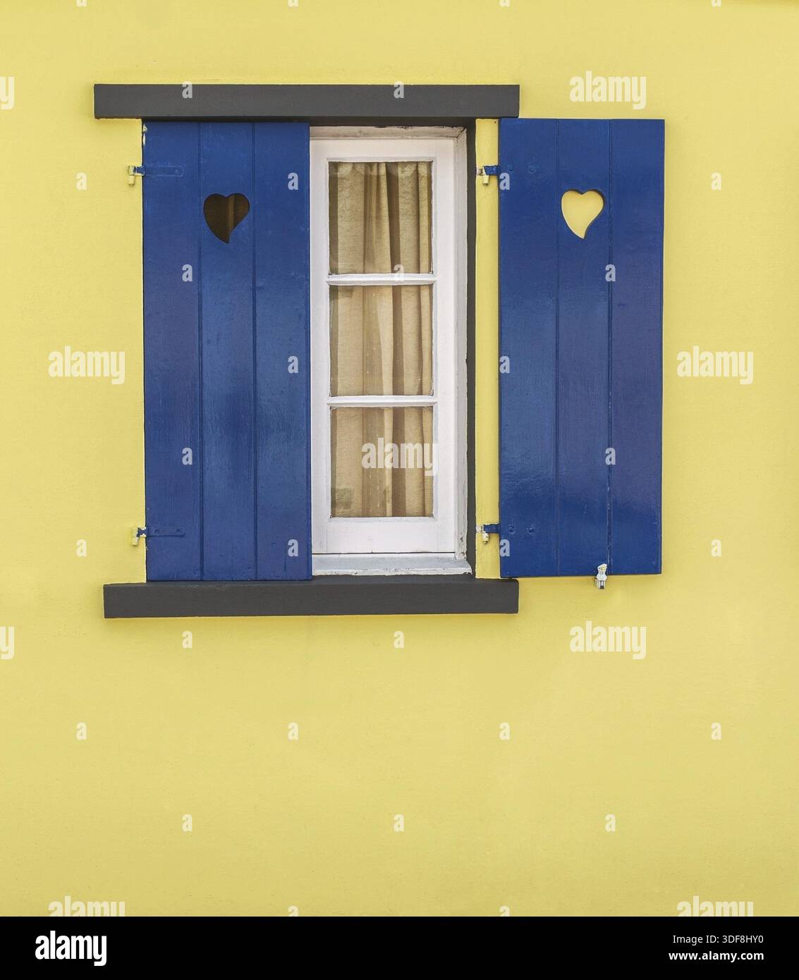 Detail des blauen Fensters mit Herzen und gelber Wand. Kostenlose Farben Stockfoto