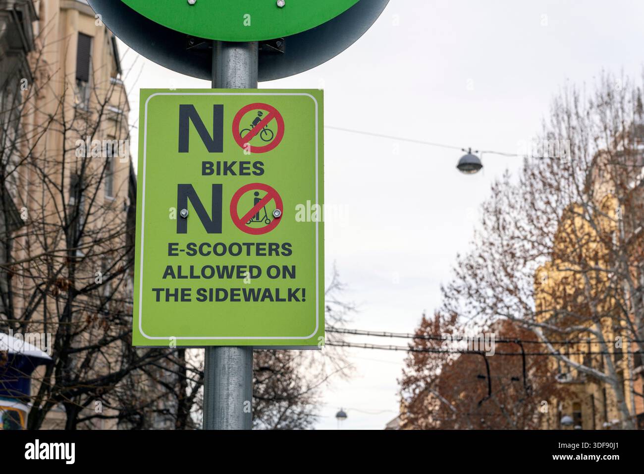 Ein Schild ist an einem Pfosten in einem Stadtgebiet angebracht. Es enthält klare Regeln, wonach Fahrräder und E-Scooter auf dem Gehweg nicht erlaubt sind. Die Szene ist Bus Stockfoto