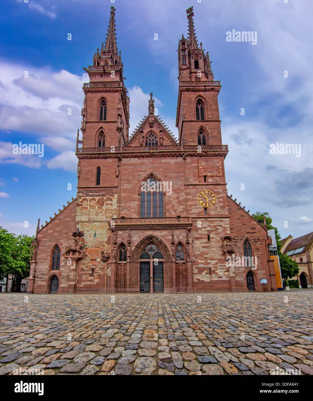 Historische gotische Kathedrale in Basel mit Doppeltürmen, Steinfassade, Kopfsteinpflasterplatz und dramatischem Himmel. Stockfoto
