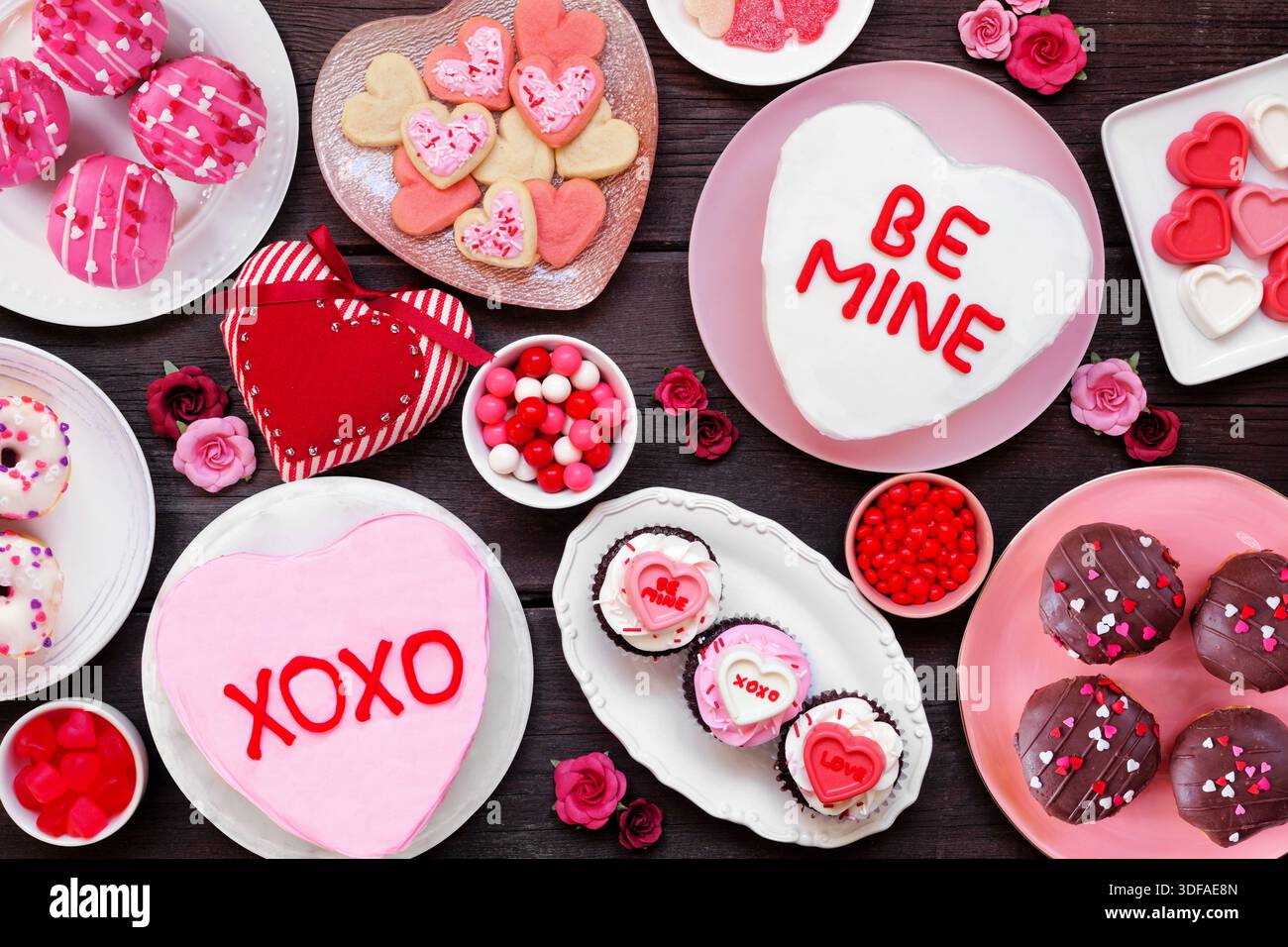 Valentinstag Tischszene mit einer Auswahl an lustigen Desserts und Süßigkeiten. Blick über dem Hintergrund aus dunklem Holz. Das Thema Liebe und Herzen. Stockfoto