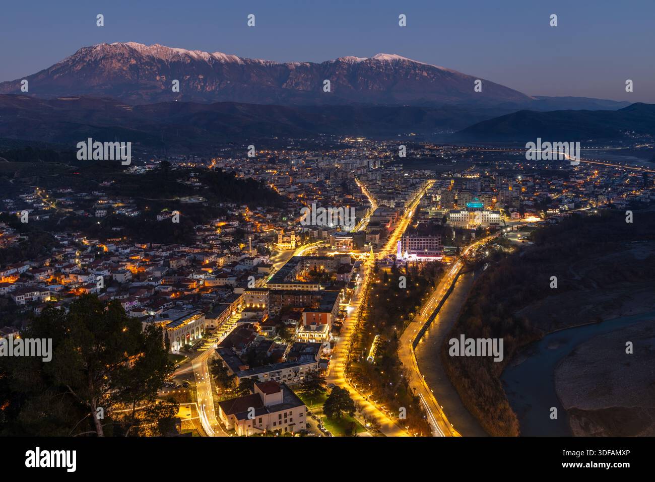 Nächtliche Stadtlandschaft mit modernen Wohngebäuden, beleuchteten Straßen, dichtem Stadtkern und schneebedeckten Gipfeln, Berat, Albanien Stockfoto