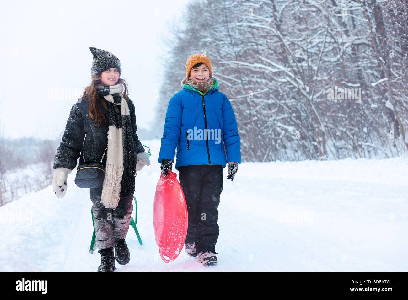 Kinder laufen mit Schlitten im verschneiten Winterpark. Kindliche Interaktion mit Bewegung, saisonaler Erholung. Winteraktivitäten, Spiel im Freien. Stockfoto