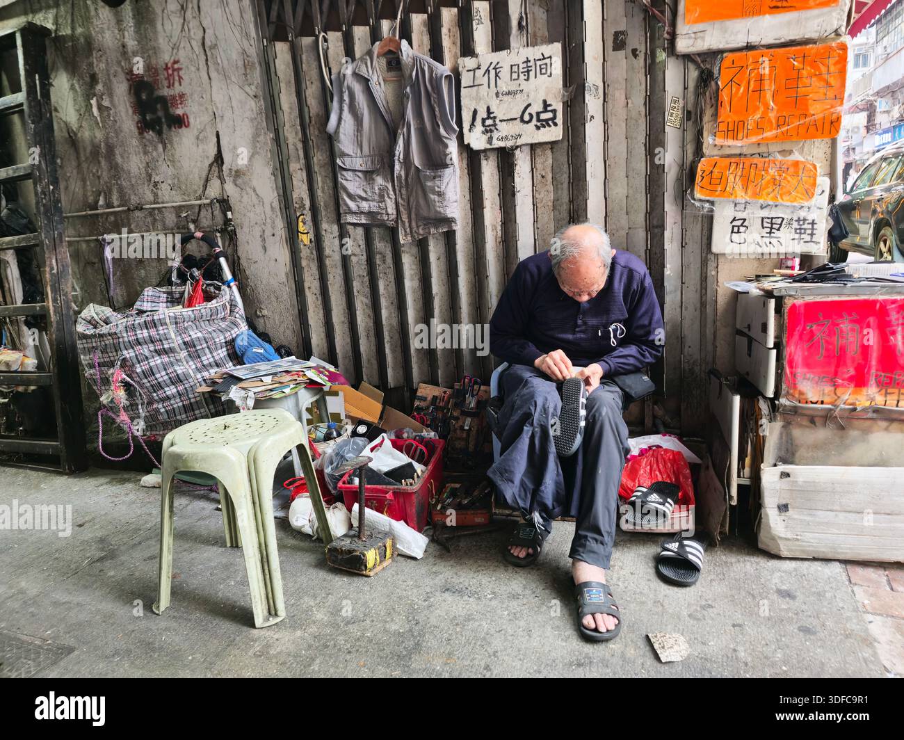 Ein älterer Schuhreparaturmann, der in einer Seitenstraße in Yau Ma Tei, Kowloon, Hongkong arbeitet. Stockfoto