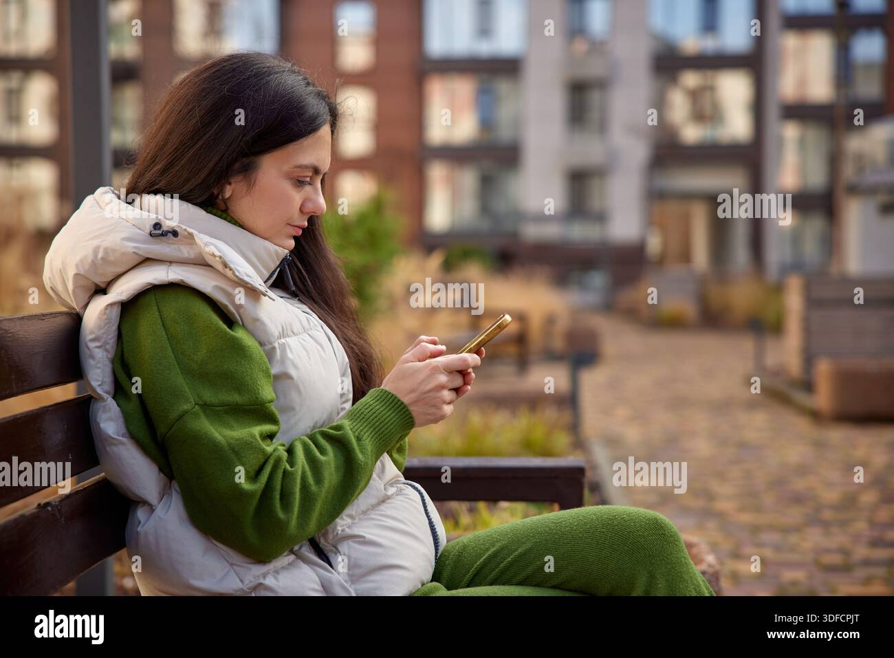 Frau, die auf einer Parkbank sitzt und auf ihrem Handy SMS schreibt Stockfoto