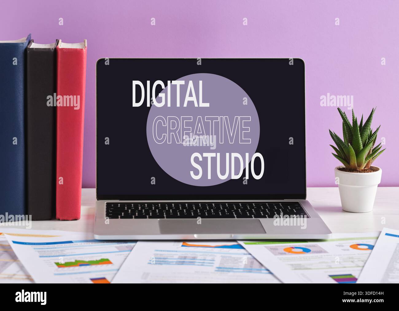 Laptop mit digitalem kreativem Studio-Schriftzug auf dem Bildschirm, auf weißem Schreibtisch mit violettem Hintergrund. Anzeigenkonzept für digitale Kreativagenturen. Stockfoto
