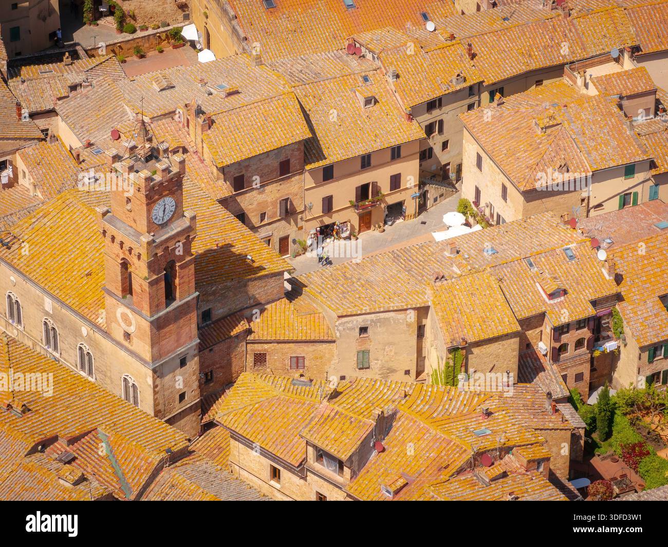 Blick aus der Vogelperspektive auf sonnendurchflutete Dächer und den berühmten Uhrturm, der Schatten über die alten Straßen von Pienza, Toskana, Italien wirft. Stockfoto