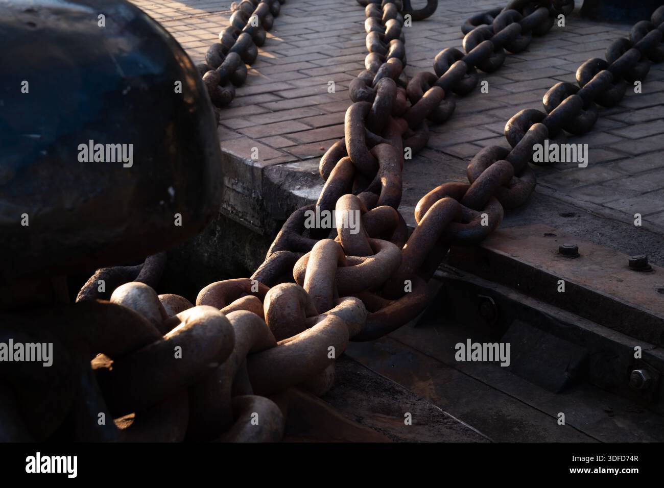 Schwere, rostige Festmacherketten, die große Schiffe an einem robusten Schiffspoller befestigen, symbolisieren Stärke, Verbindung und Schiffsindustrie auf einem Hafendock Stockfoto