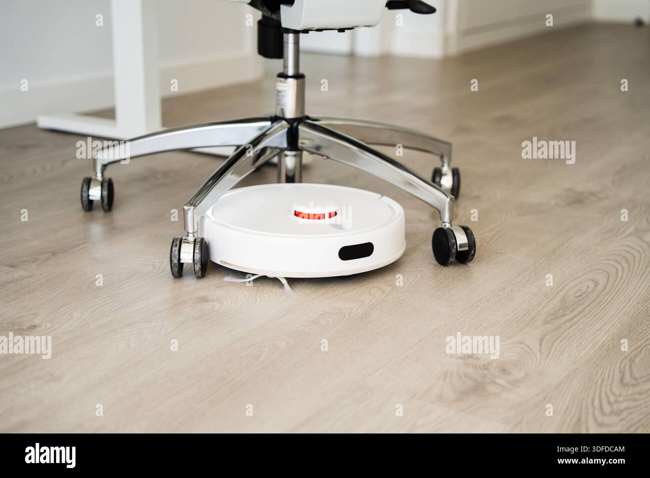 Intelligenter Roboter-Staubsauger, der unter Bürostuhl auf Holzboden arbeitet, automatisches Reinigungsgerät für moderne Heim- und Arbeitsbereiche Stockfoto