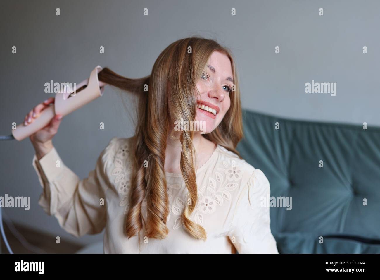 Lifestyle-Schönheitsbild einer lächelnden Frau mit Haarstyling-Werkzeug in minimalem gemütlichem Innenraum Stockfoto