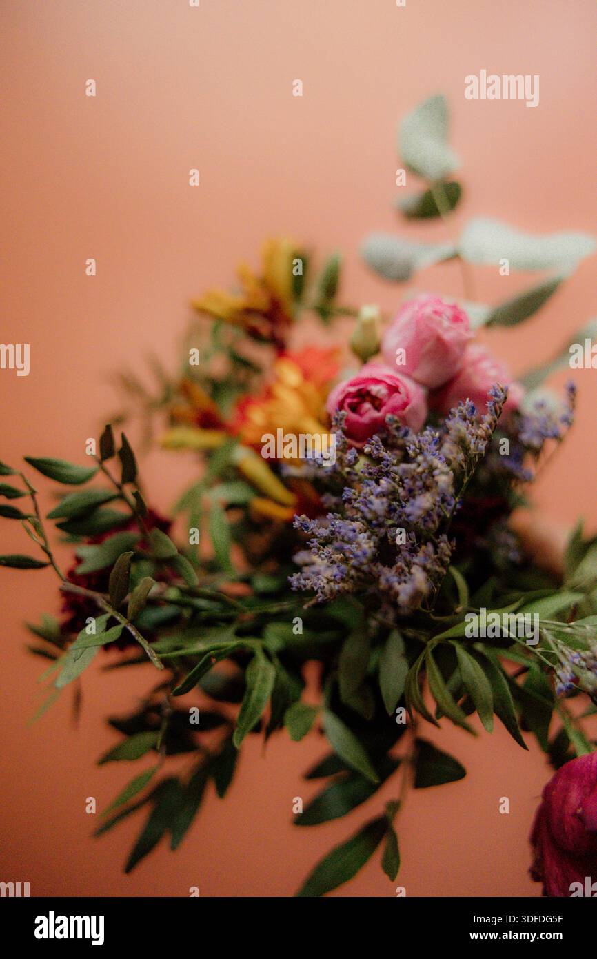 Hand hält bunten Blumenstrauß vor warmem Pastellhintergrund Stockfoto