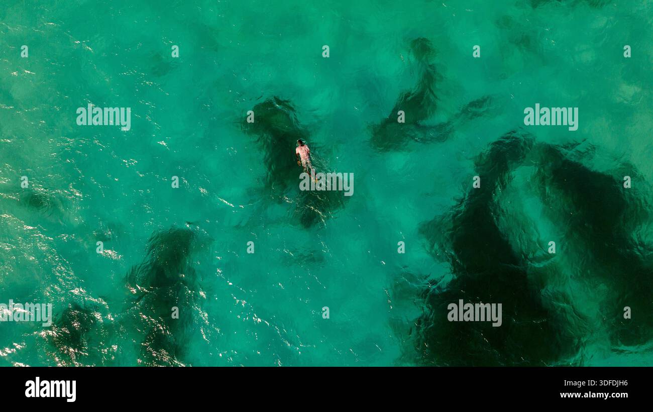 Pemba, Mosambik - 2. Juli 2025: Aus der Vogelperspektive eines einsamen Schwimmers, der durch das kristallklare türkisfarbene Wasser navigiert, im Kontrast zum dunklen, untergetauchten Ro Stockfoto