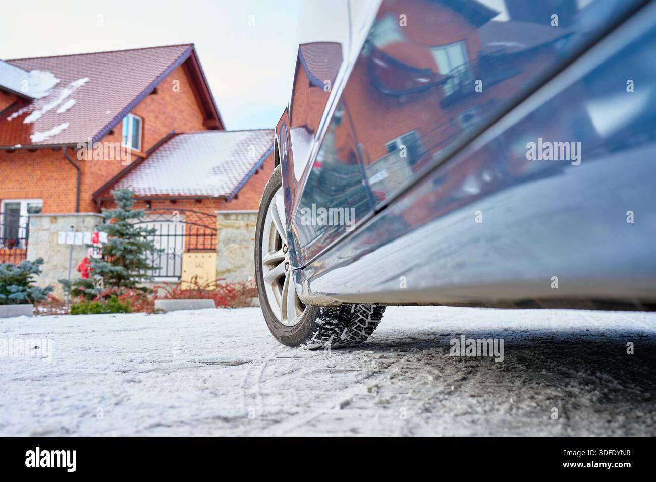 Flacher Blick auf das Autorad mit Winterreifen auf verschneite Straße in der Nähe eines Wohnhauses. Konzept für Winterfahren, Straßensicherheit, kalte Witterungsbedingungen und Stockfoto