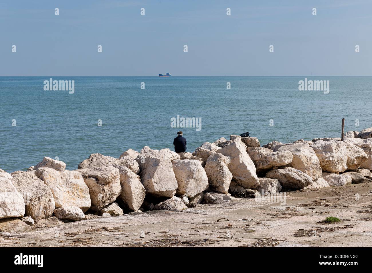 Rückansicht eines Seniorenmannes, der am Meer sitzt und den Horizont über dem Wasser betrachtet und dabei Freiheit, Urlaub oder Altersvorsorge genießt Stockfoto