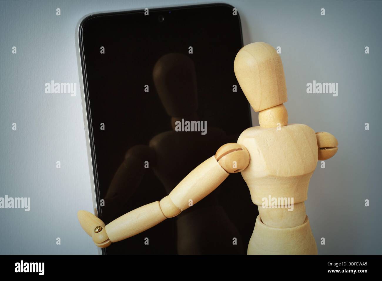 Hölzerne Schaufensterpuppe mit Blick auf seine Reflexion auf einem Smartphone-Bildschirm - Konzept von Identität, Selbstwahrnehmung und sozialen Medien Stockfoto