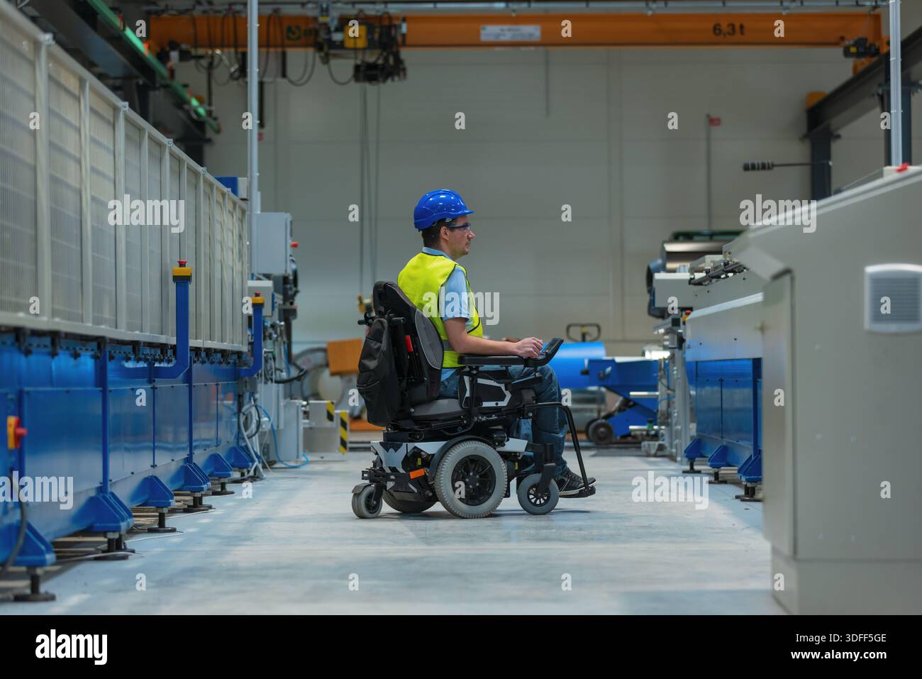 Fachkräfte mit Behinderungen bedienen eine Maschine, während sie einen Rollstuhl in einer Fabrik benutzen, die für Zugänglichkeit ausgelegt ist. Stockfoto