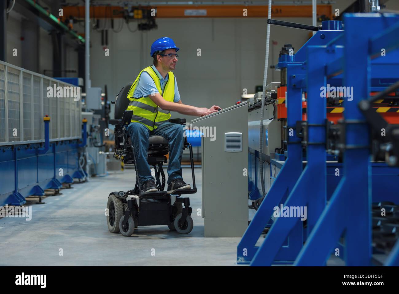 Arbeitnehmer mit Behinderungen, die einen Rollstuhl benutzen, bedienen eine Industriemaschine in einem Fabrikbetrieb, der auf integrative Beschäftigung und Sicherheit ausgerichtet ist. Stockfoto
