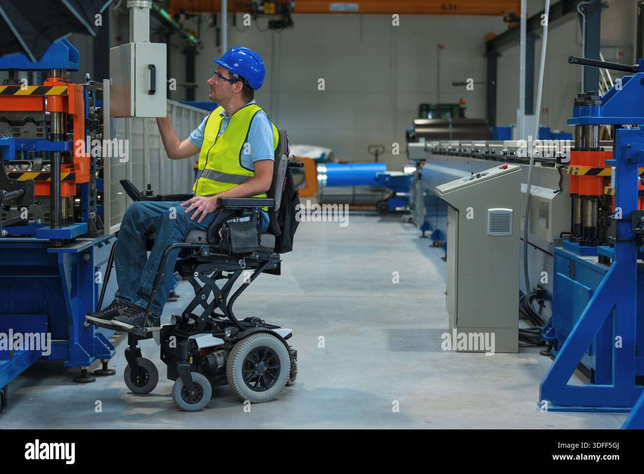 Ein behinderter Arbeiter bedient eine Industriemaschine in einer modernen Fertigungsumgebung mit einem Rollstuhl. Stockfoto