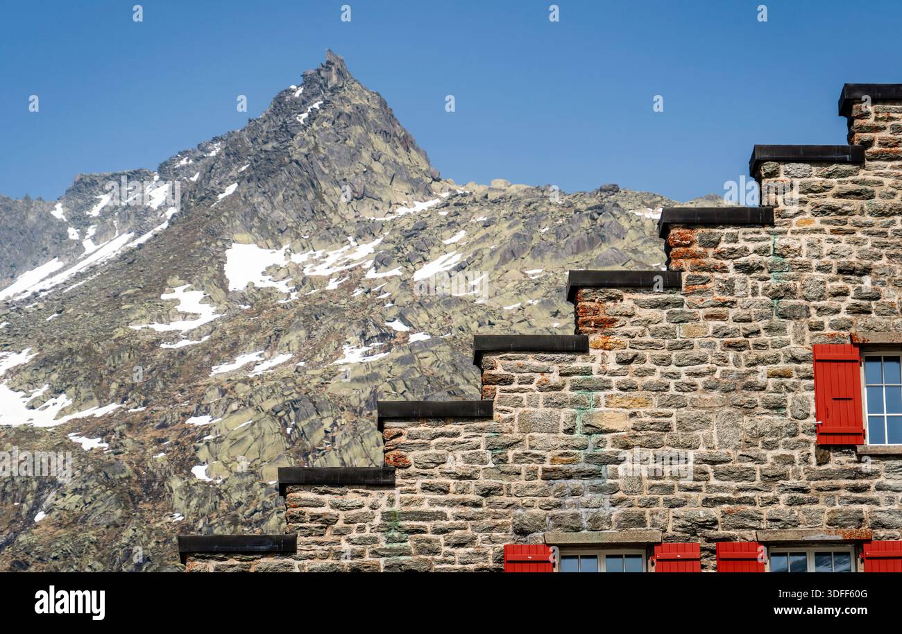 Steingebäude mit roten Fensterläden vor Bergkulisse. Stockfoto