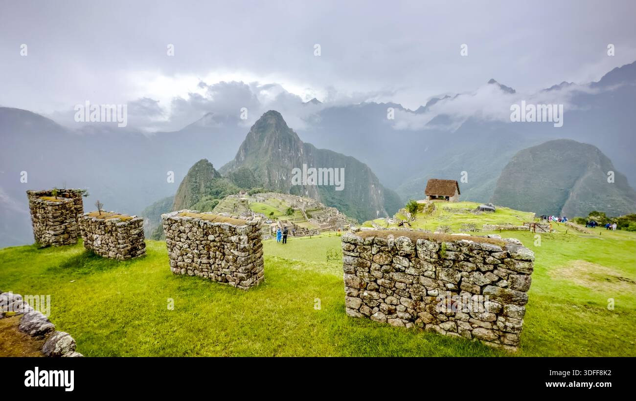 Der Blick auf die alten Steinmauern führt den Blick in Richtung des berühmten Berges Huayna Picchu in der Ferne, umgeben von Nebel und Rätsel, Machu Picchu, Peru. Stockfoto