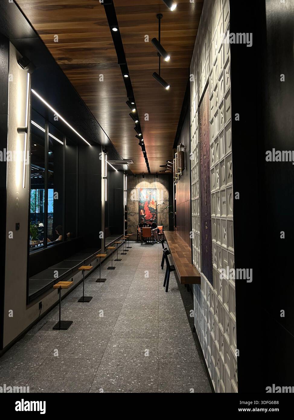 Innenansicht eines modernen Restaurantkorridors mit langer Perspektive mit Holzdeckenpaneelen, linearen Deckenleuchten, strukturierten Wänden, Bänken, Stockfoto