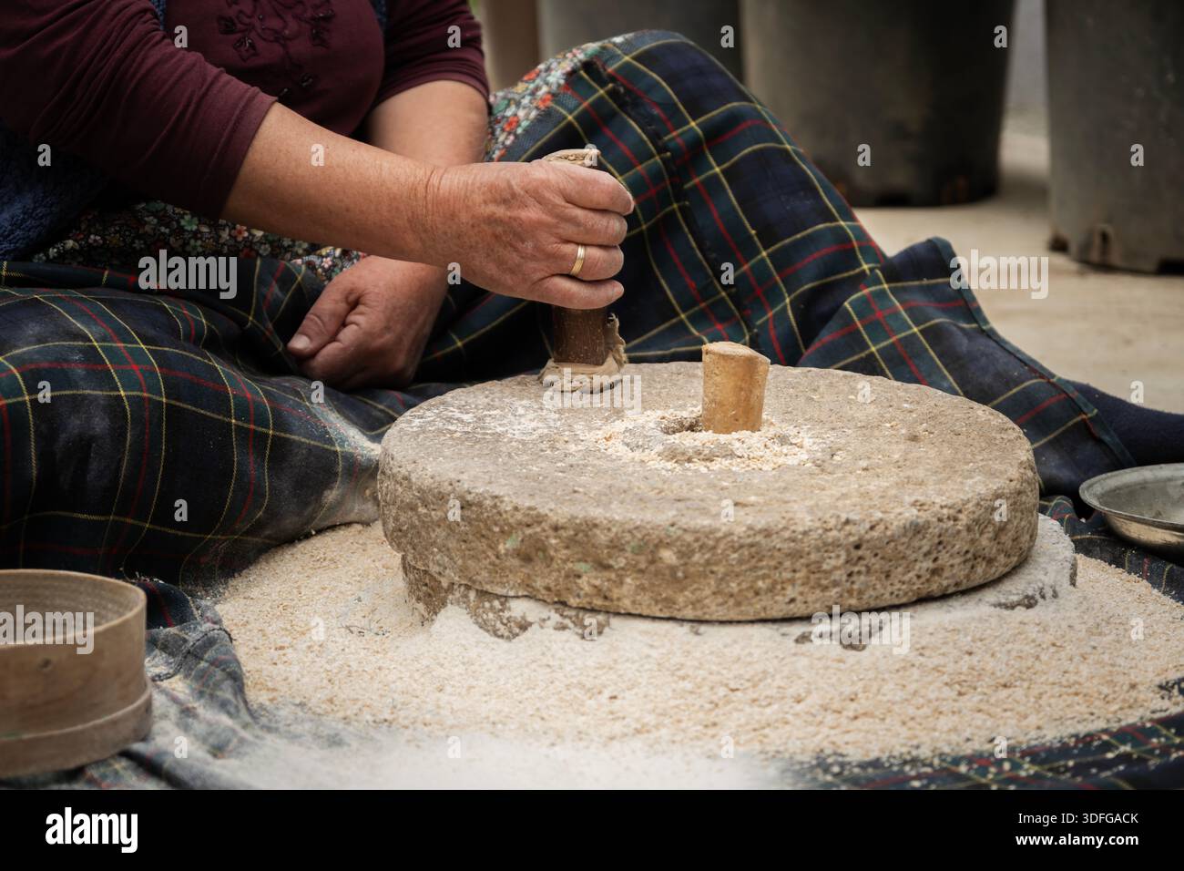 Ältere Frau mahlt Vollkornmehl zu Mehl mit einer traditionellen Steinmühle, die die alte Landwirtschaft und die natürliche Lebensmittelzubereitung widerspiegelt Stockfoto