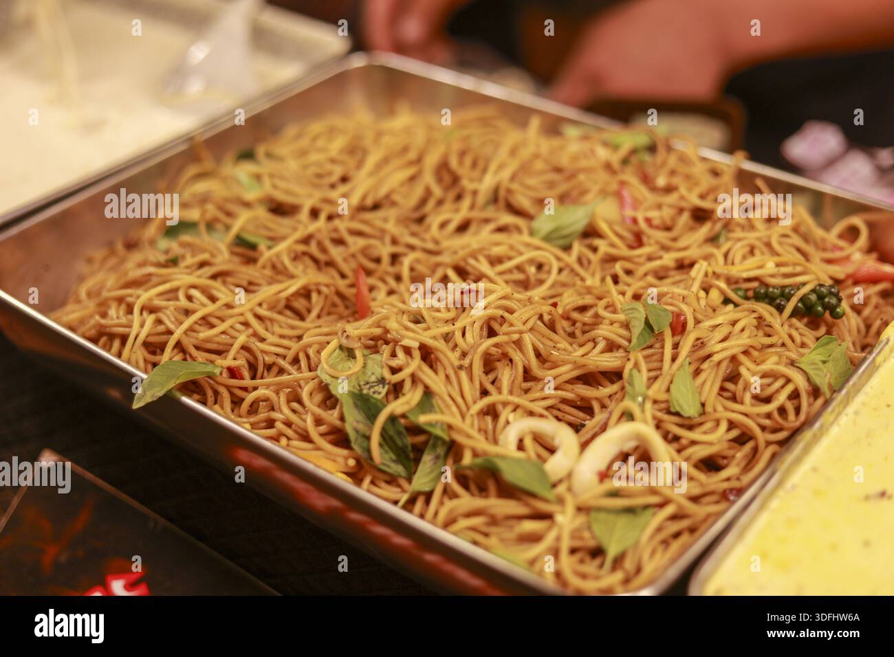 Köstliche gebratene Nudeln mit Basilikum- und Tintenfischringen in Metalltablett, bereit für Partybuffet oder Mittagessen Catering Service sieht lecker aus und schmackhaft für das Restaurant Stockfoto